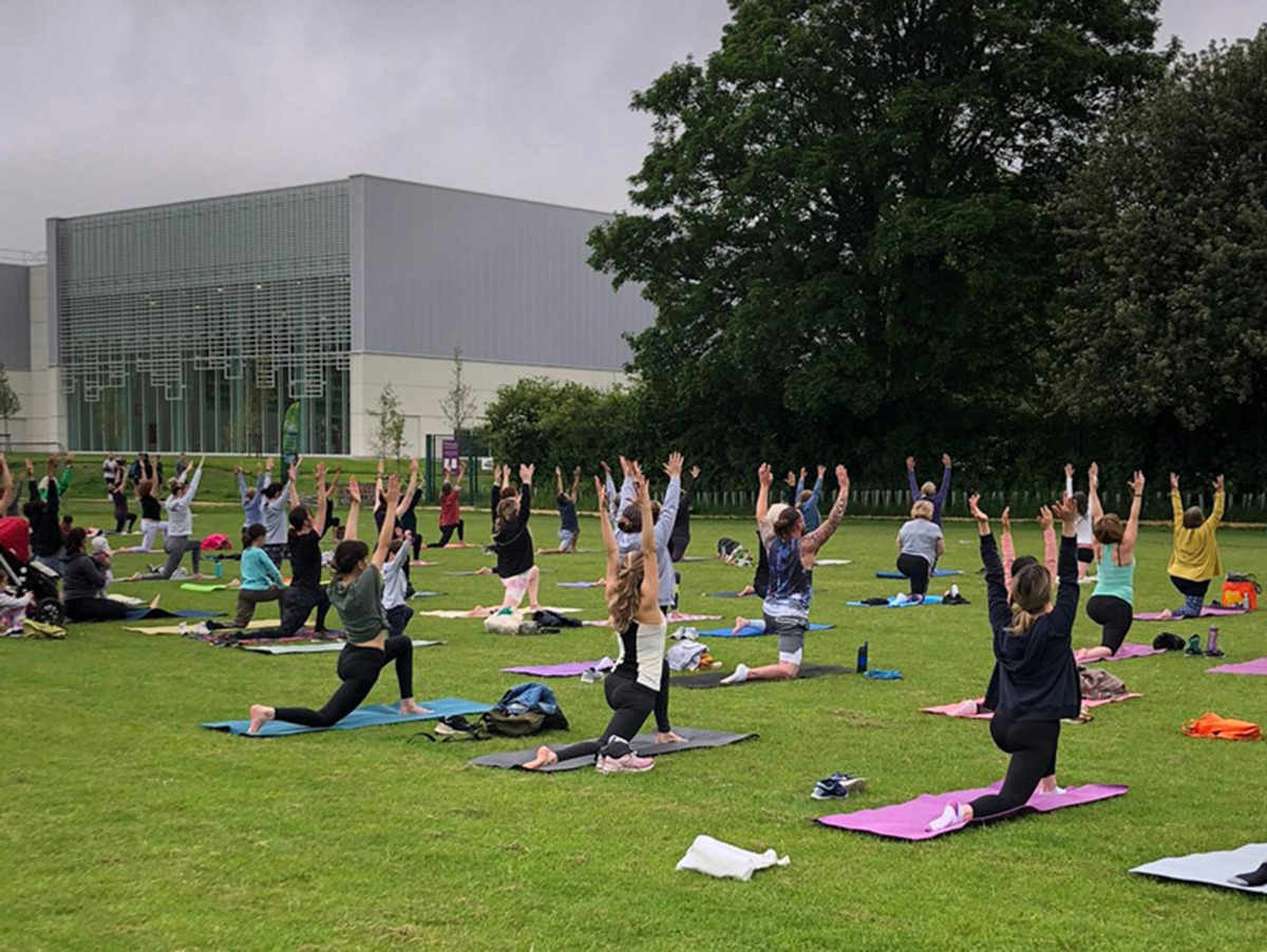 A large group of people participating in Park Yoga outdoors in a green space near a building inWinchester 