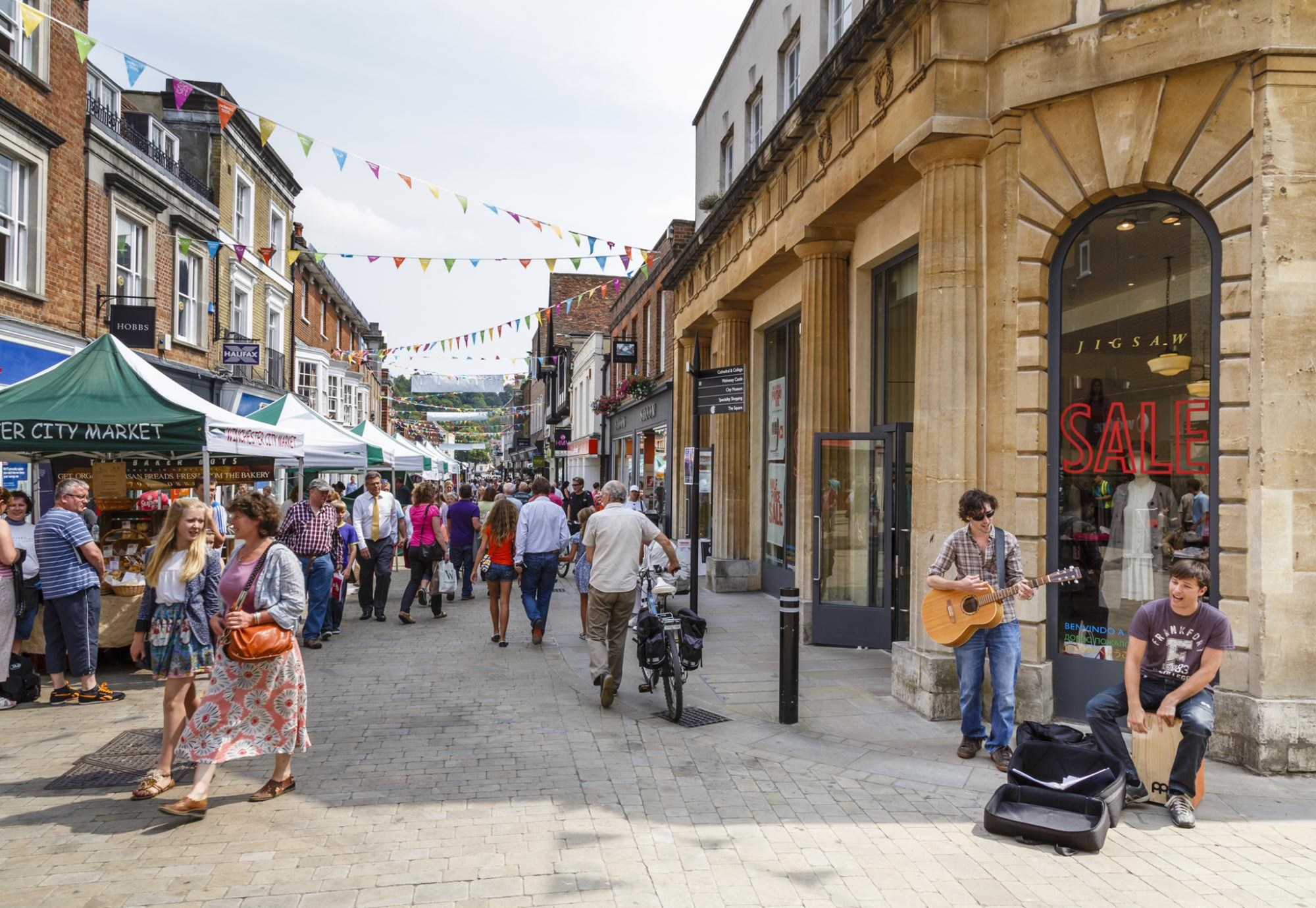View looking down the street market, including green and white gazebos and people walking through