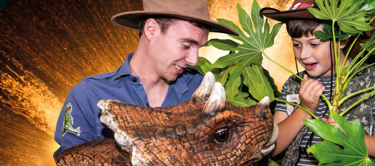 article thumb - Photo shows an Inpsirer dressed as a ranger, Trixie the dinosaur, and a young boy amongst leaves.