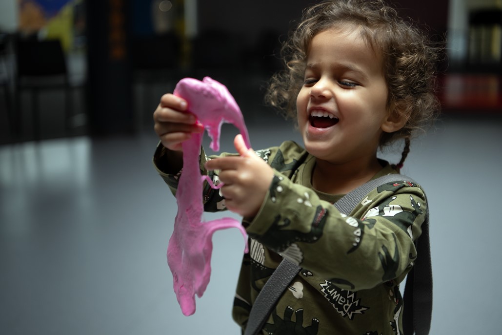 article thumb - A young girl holding pink slime. The girl is looking at the slime with a big smile on her face.